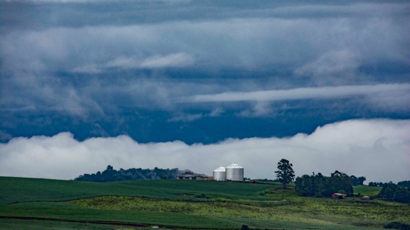 Nuvens carregadas de chuva, campo verde e silos de metal